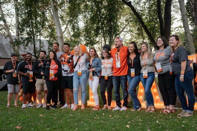 A large group of alumni stand in front of Pacific sign.